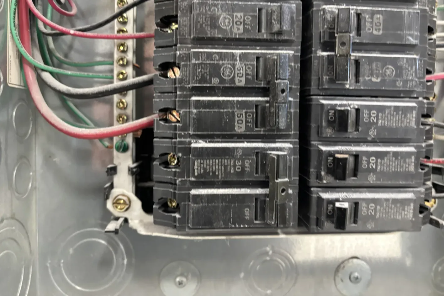 Inside an electrical panel, rows of GE breakers with wires landed on the terminals and the ground bar on the left