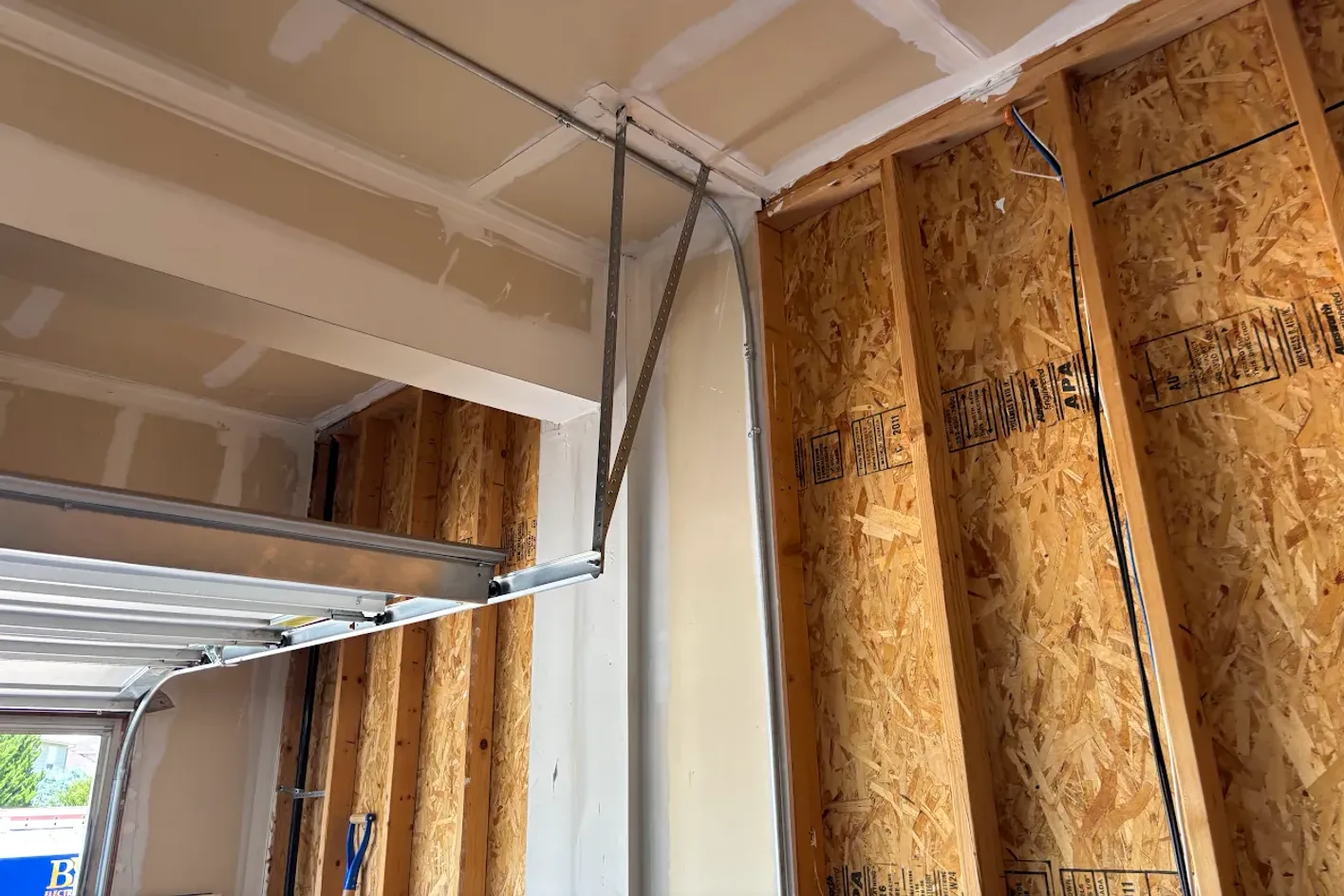 Open wall framing in a garage with the garage door track overhead, where a dedicated charger circuit would be run