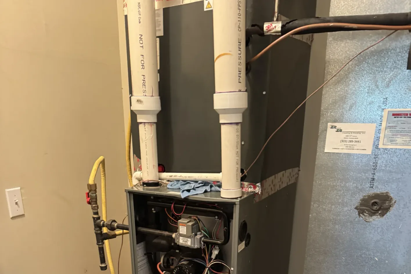 A gas furnace in a utility closet with the gas line, venting, and the service panel open for inspection