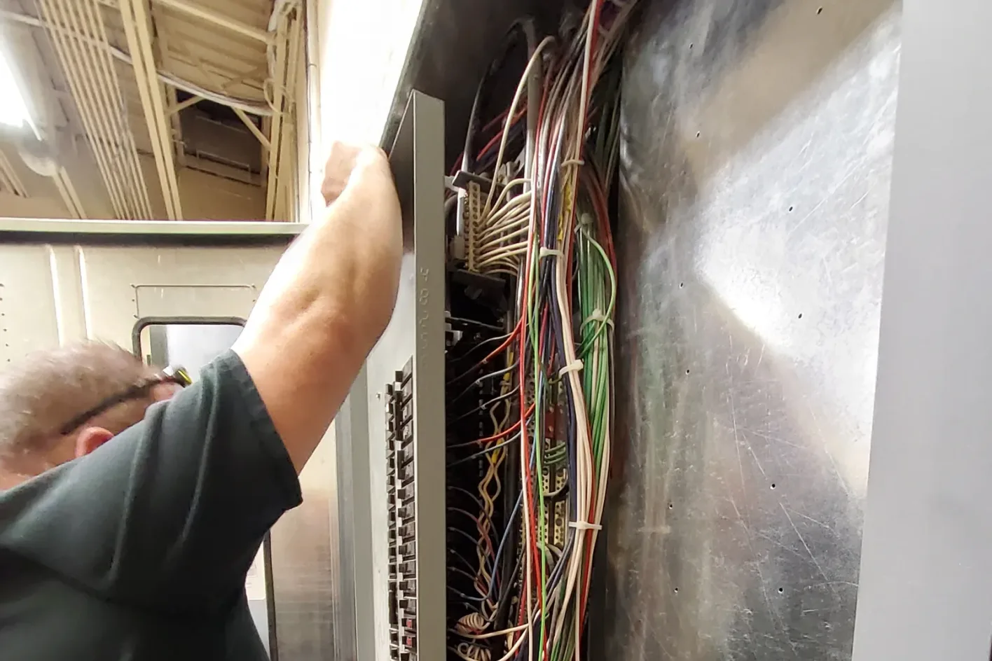A BES electrician reaching into an open electrical panel with a dense bundle of wires visible inside